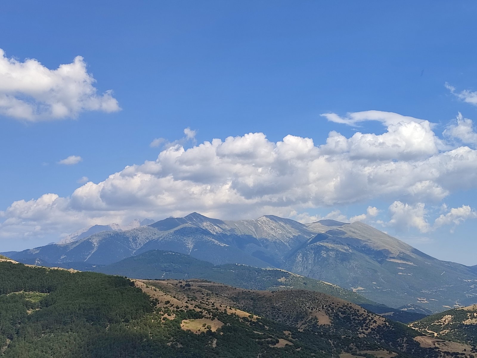 Majestic snow-capped peak of Mount Olympus rising above dramatic clouds at golden hour