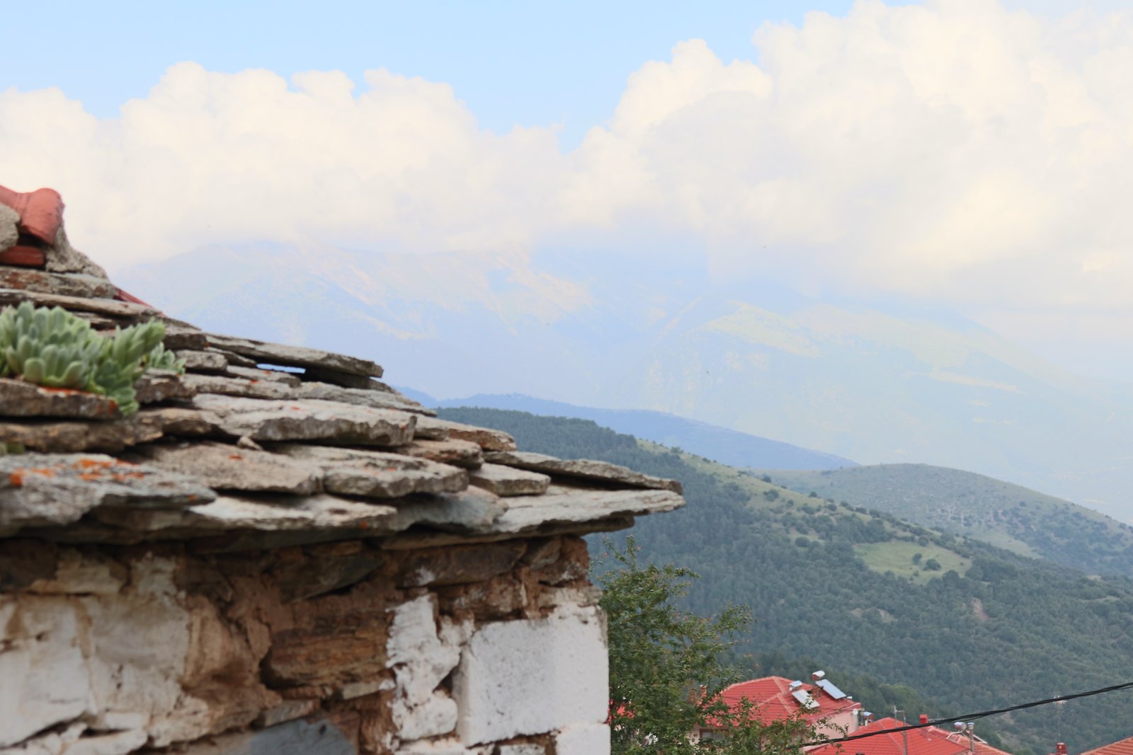 Traditional stone mountain village with red-roofed houses nestled against a green mountainside