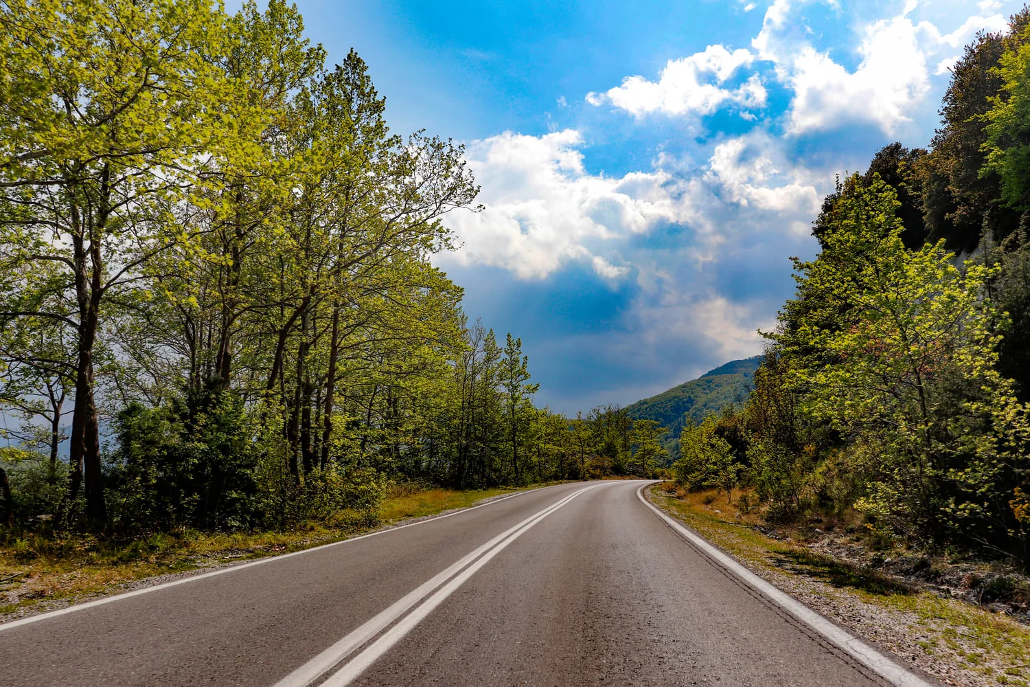 A winding mountain road through lush green hills leading toward Mount Olympus